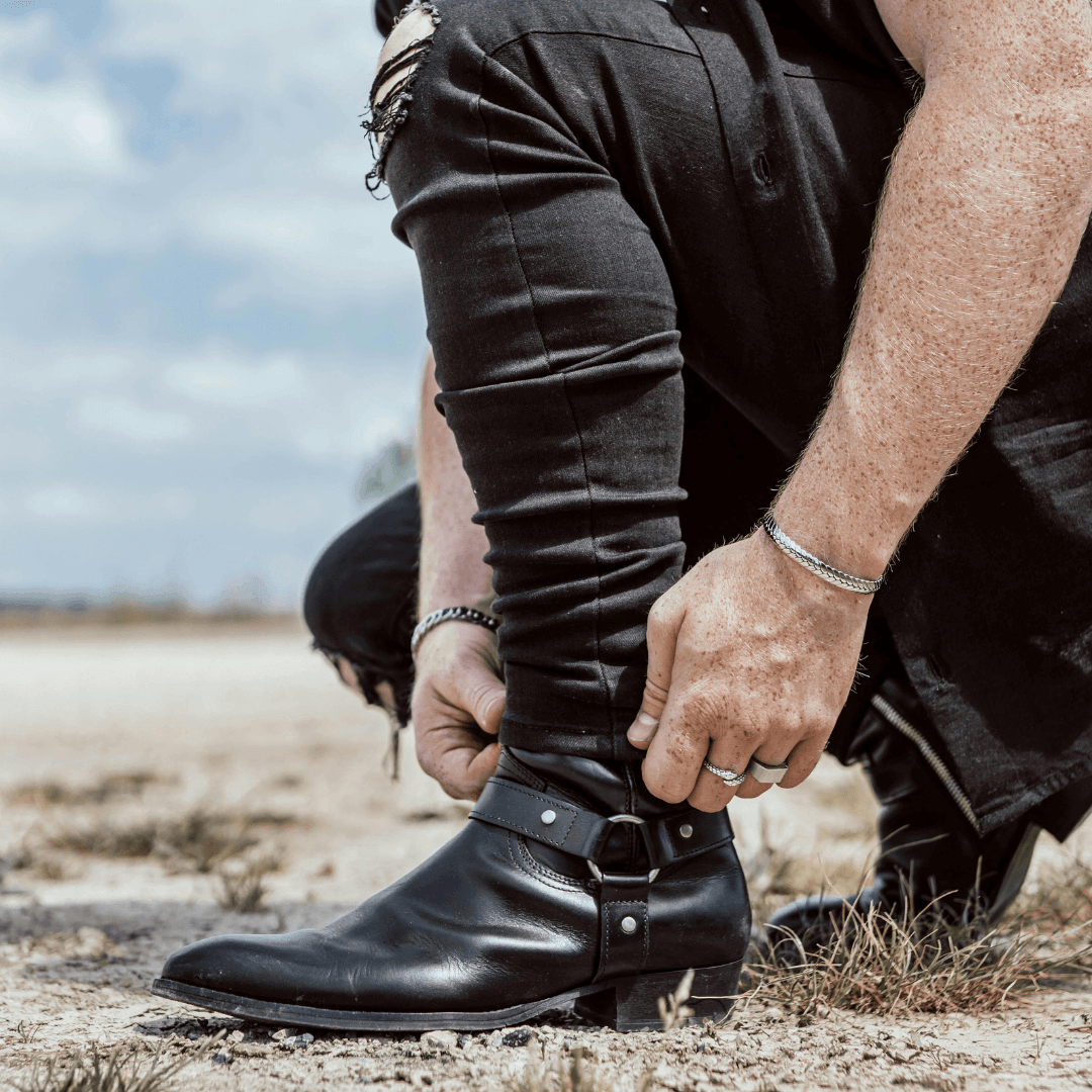 Man tying up black leather boots outdoors, showcasing durable footwear and style.